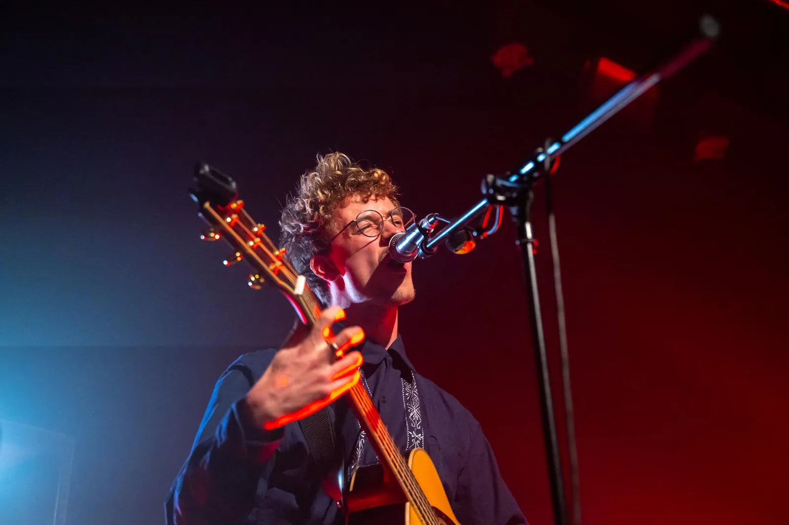 Musiker mit Gitarre am Mikrofon auf der Bühne im roten Licht