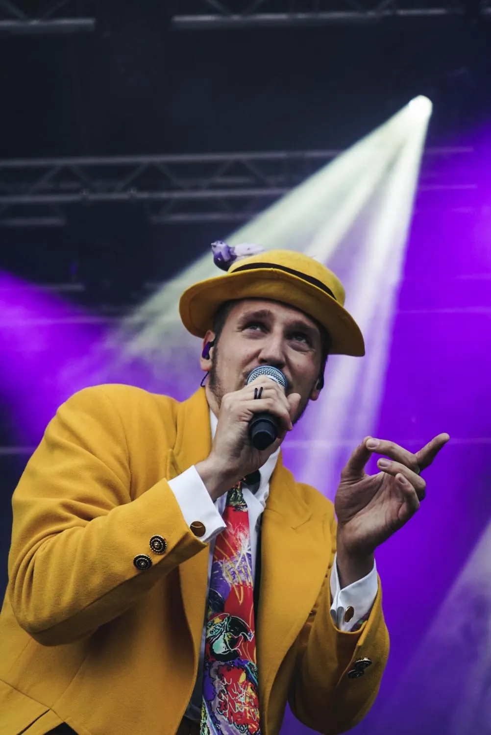 Sänger in gelbem Jackett und Hut auf der Bühne im violetten Scheinwerferlicht